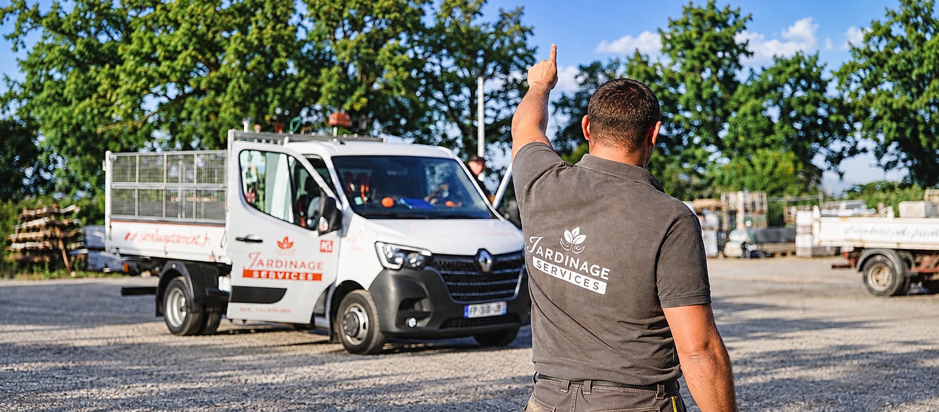 Un homme vu de dos, portant un polo gris marqué Jardinage Services, lève le bras devant une camionnette blanche à benne.